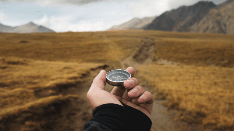A person using a compass on a path that leads far into the distance though mountains.