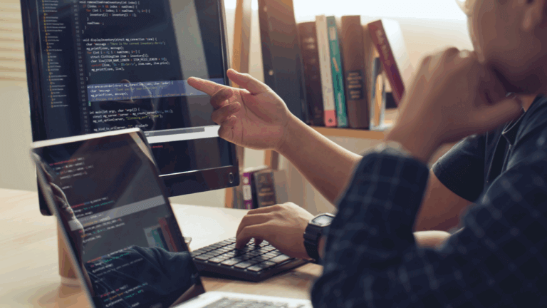 Two coworkers sit at a desk reviewing website code together.