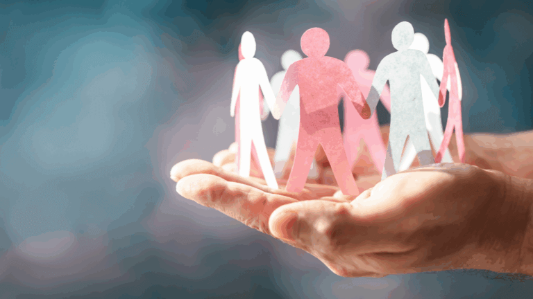 A closeup of hands holding human figures holding hands in a circle cut from paper.