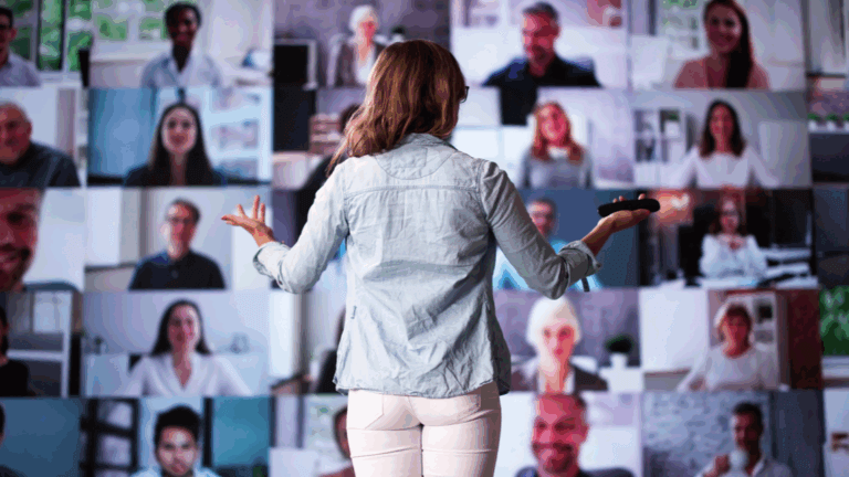 A woman giving a remote presentation in front of a large screen showing participants.