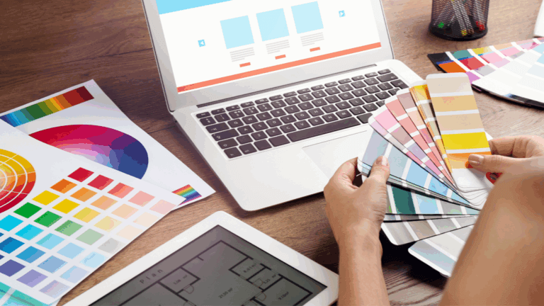 Designer selecting brand colors from swatches while reviewing website mockups on laptop.