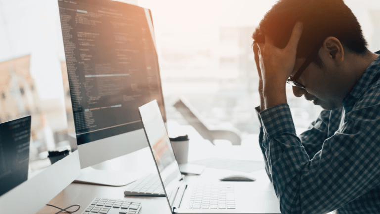 Frustrated web developer working on a laptop at his desk.