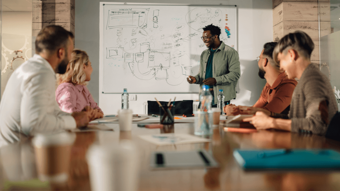 Startup founders working together at a table with a whiteboard reviewing product diagrams.